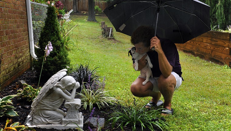 HALETHORPE, MD - SEPT 24: Jim Schenning (holding his new dog Kate) visits the memorial for his previous dog Emma. The memorial is just outside of his office, a place he chose to be closer to Emma. Schenning had Emma put down at his home in May by a vet who specializes in home euthanasia. He got his new Jack Russell, Kate, a few weeks ago.(Photo by Michael Williamson/The Washington Post via Getty Images)