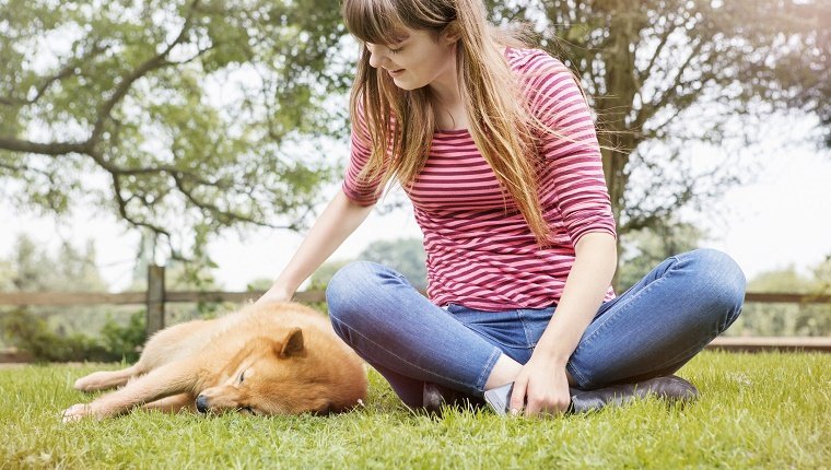 yung woman strokes dog snoozing in grass.