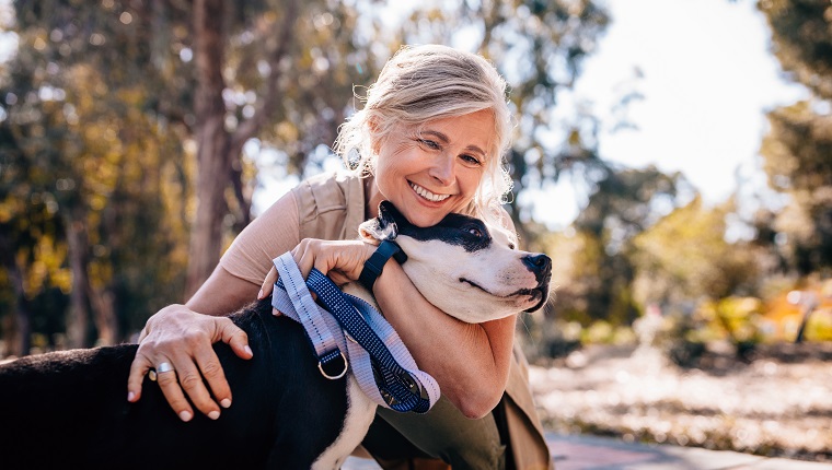 Happy senior woman enjoying walk in nature and embracing pet dog in forest park