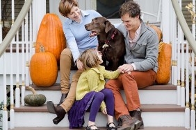 Happy Family Sitting In Front of House with Dog and Pumpkins