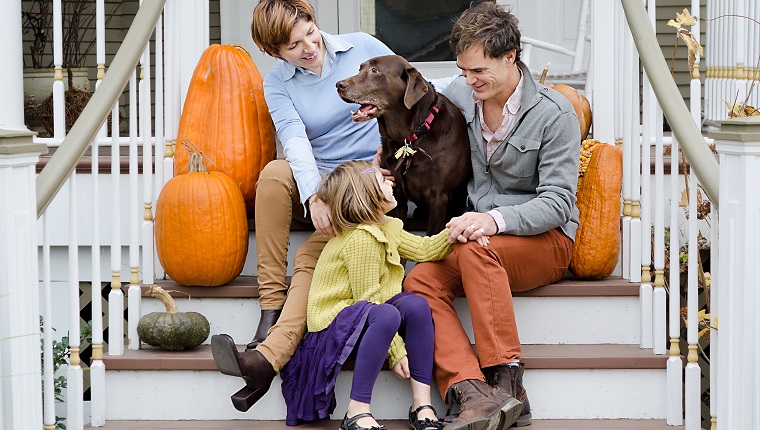 Happy Family Sitting In Front of House with Dog and Pumpkins