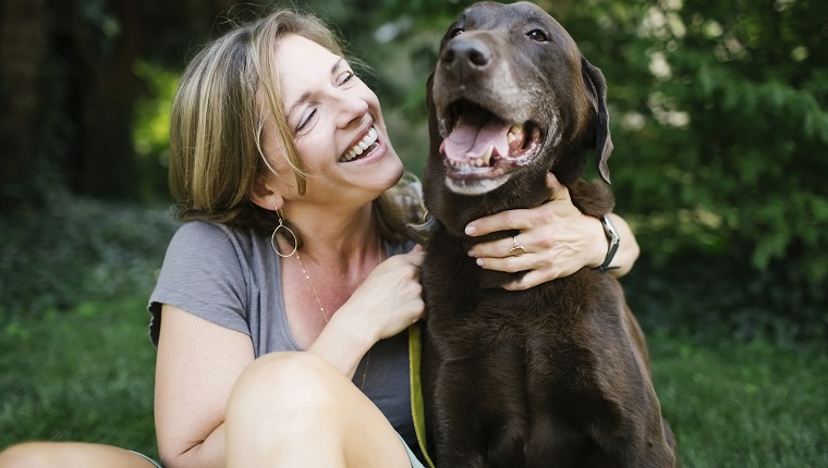 Smiling woman sitting on grass with Labrador Retriever