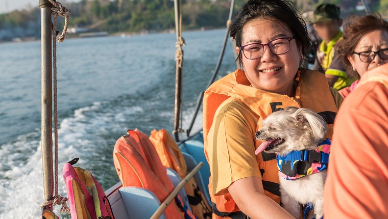 Asian woman and dog so cute mixed breed with Shih-Tzu, Pomeranian and Poodle sailing on Songkaria river by long tail boat with sun light in evening time when vacation travel for relax