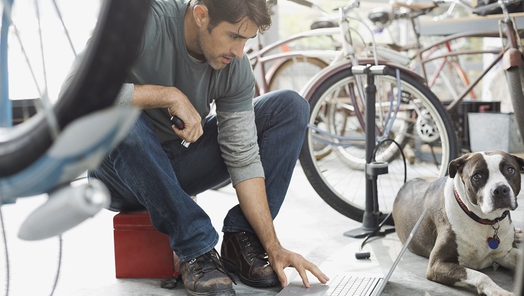 man with dog and computer in bike shop