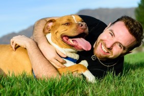 Happy male with his dog on the grass. Mountain range and clear sky in background.