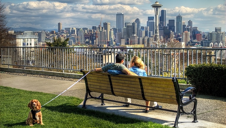 Man and woman sitting on park bench with dog on leash.