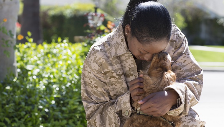 Female soldier hugging pet dog on street at homecoming