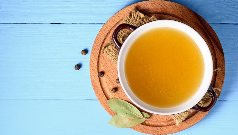 Chicken broth in ceramic bowl on blue wooden background. Top view.