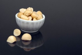 A small snack-size bowl of macadamia nuts (or ingredient size bowl) sits on a black reflective surface.