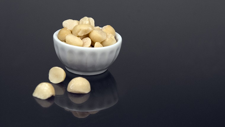 A small snack-size bowl of macadamia nuts (or ingredient size bowl) sits on a black reflective surface.