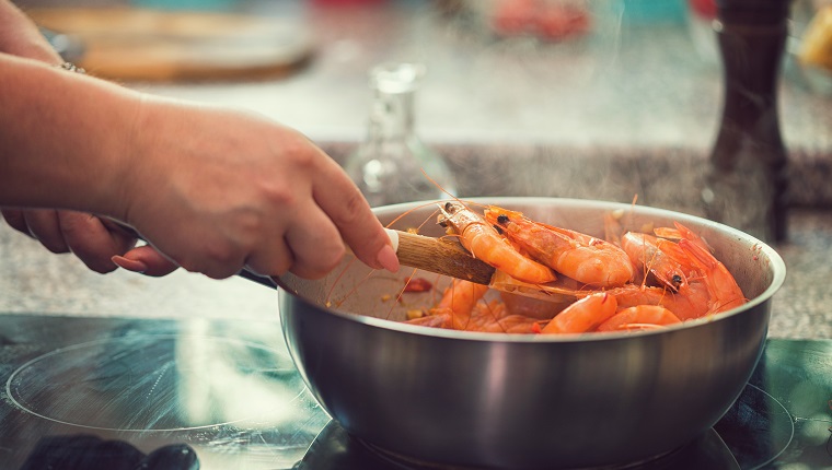 Young women preparing shrimps with white wine,chili pepper and parsley at home