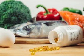 Supplement Bottle with Gel Capsules On a Wooden Table. Natural Food Sources of Vitamin D In Background.