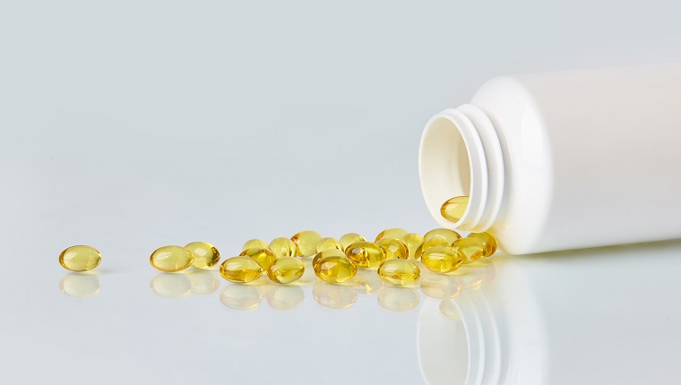 Fish oil capsules scattered from white plastic bottle on white background.  Health care concept.