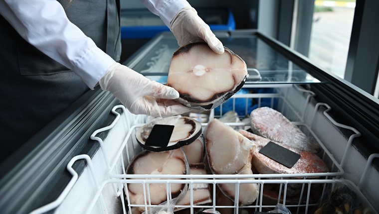 Fishmonger holding a piece of frozen sea shark fillet. A fish vendor in a seafood market taking a frozen fish steak out of the refrigerator