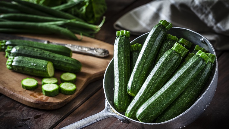 Fresh organic zucchini in an old metal colander shot on rustic wooden table. This vegetable is considered a healthy salad ingredient. Predominant colors are green and brown. Low key DSRL studio photo taken with Canon EOS 5D Mk II and Canon EF 100mm f/2.8L Macro IS USM