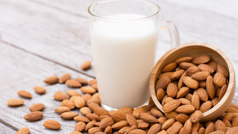 Almonds nuts in wooden bowl and almond milk in glass on wood table background.