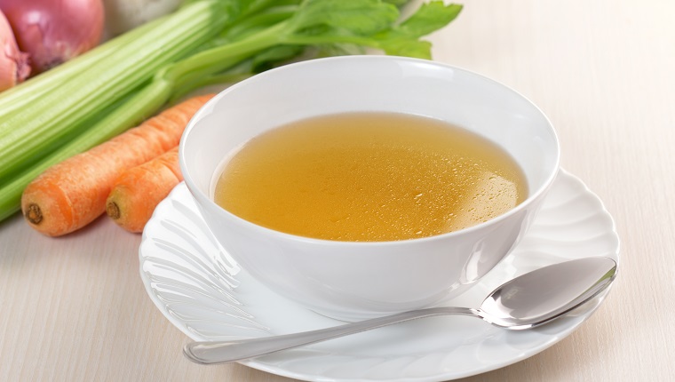 bowl of broth and fresh vegetables on wooden table