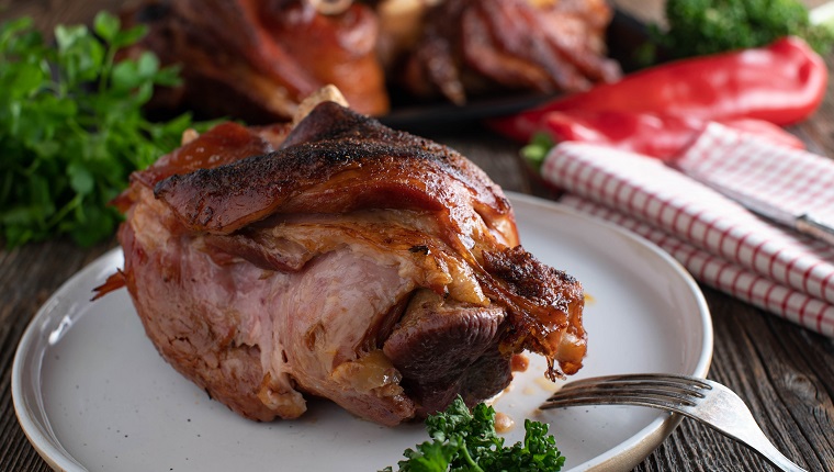 Traditional german meat dish with ham hock or pork knuckle fresh oven baked and served on a plate on rustic and wooden table background. Closeup and front view