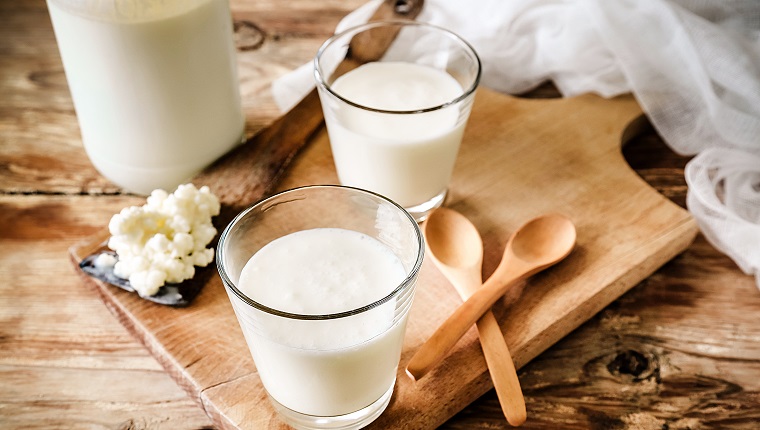 Organic probiotic milk kefir grains, Tibetan mushrooms, kefir grains in wooden spoon with glass of kefir. Rustic table setting, wooden table, spoon and cutting board.