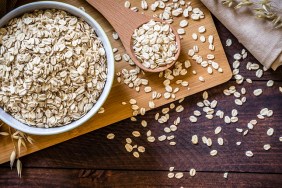 Top view of a bowl filled with uncooked oat flakes with a wooden spoon on wooden table. There is a useful copy space in the lower right corner