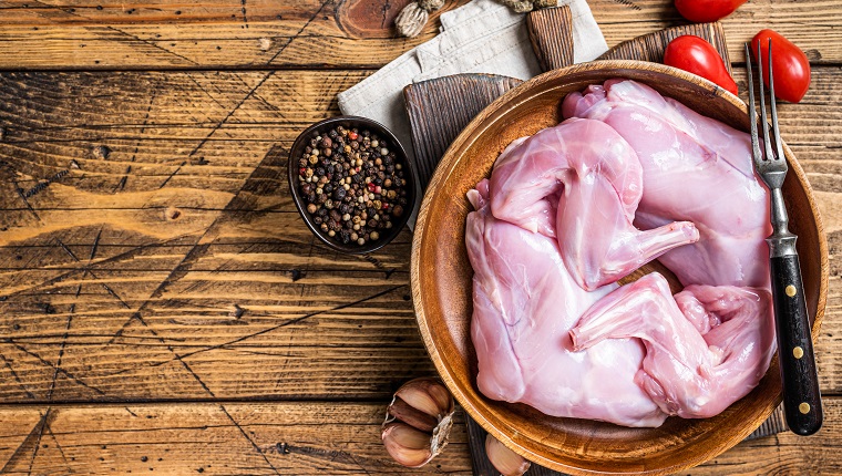 Rabbit legs uncooked in a wooden plate. Wooden background. Top view. Copy space.