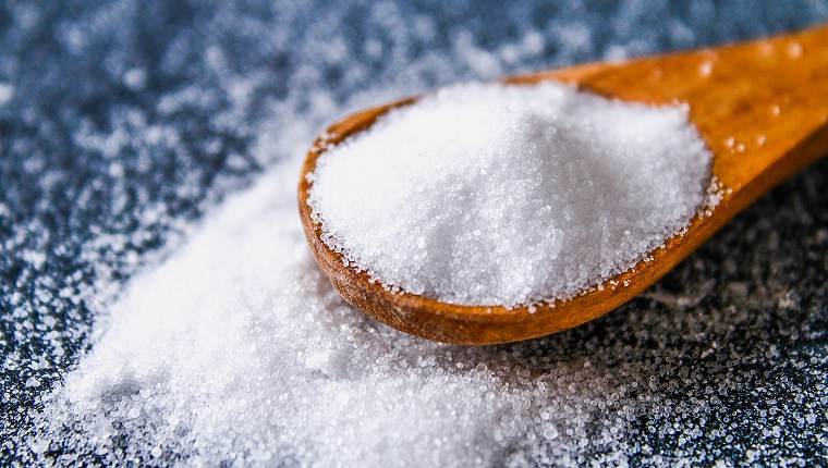 Crystals of shallow salt in a scoop, spoon on a dark gray table. Background for advertising salt. Table salty. Salted food