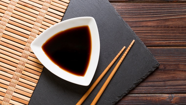 Chopsticks and soy sauce on black stone plate, wooden background with copy space.