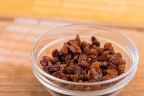 Bowl of raisins. Sultana raisins in glass bowl. Wooden chopping board. Yellowish background. Light effect. Selective focus.