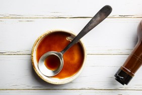 Worcestershire sauce in a bowl with spoon and bottle over white background, top view