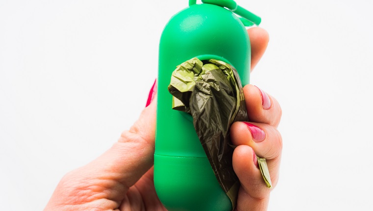 Compostable dog poop bags dispenser in woman's hand on white background. Eco friendly solution for pet owners