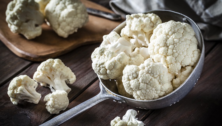 Fresh organic cauliflower in an old metal colander shot on rustic wooden table. This vegetable is considered a healthy salad ingredient. Predominant colors are white and brown. Low key DSRL studio photo taken with Canon EOS 5D Mk II and Canon EF 100mm f/2.8L Macro IS USM