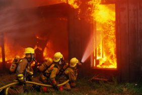 Three firefighters holding a water hose as they extinguish a burning house, like the ammunition-fueled house fire in Sylmar.