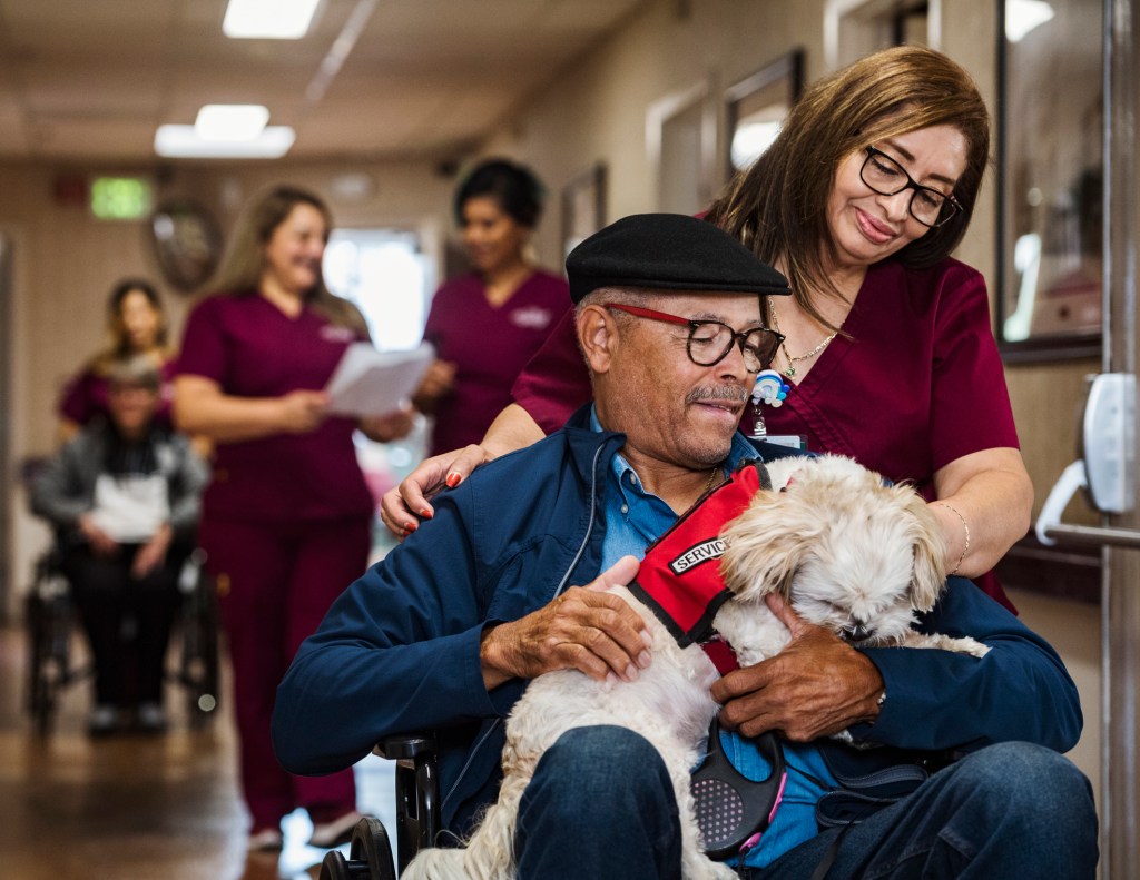 Nurse assisting senior man in wheelchair holding service dog