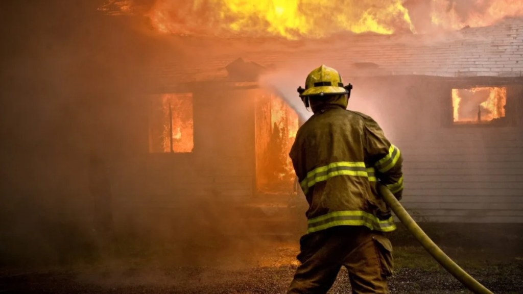 Firefighter spraying water at a house fire.