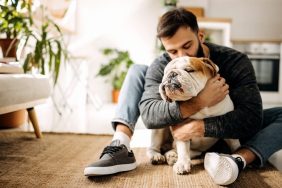 Photograph of a young man hugging his English Bulldog, a smart dog breed choice for a dog-friendly condo.