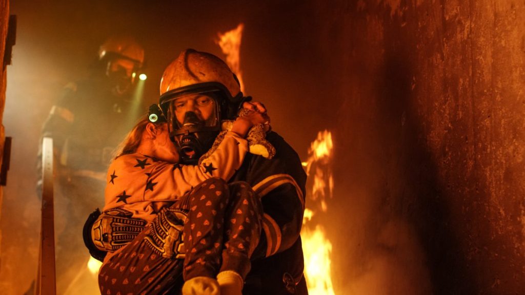 A firefighter holding a little girl in his arms, like the girl who was reported dead while trying save her dog from house fire.