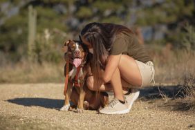 A woman kissing and holding her pet pit bull while having fun outdoors. Young woman expressing love and affection for her emotional support animal.