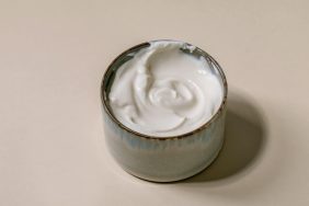 Sour cream, which dogs can eat safely in moderation, in ceramic bowl over beige background.