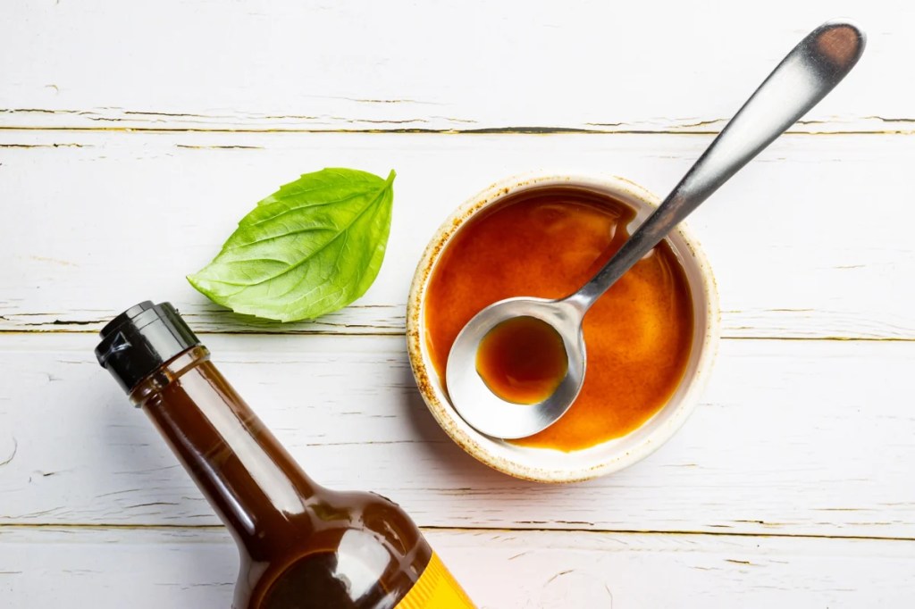 Worcestershire sauce, which dogs cannot eat, in a bowl with spoon and bottle over white background, top view