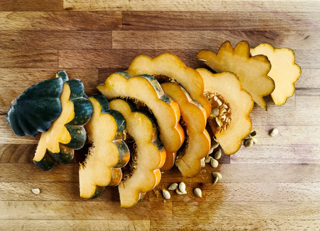 A photo of sliced acorrn squash, which is safe for dogs to eat if cooked, on a wooden cutting board.