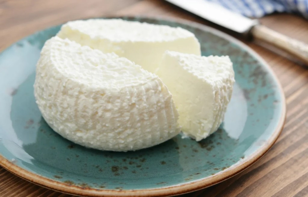A close-up photo of fresh ricotta cheese, which can be safe for dogs to eat in moderation, on a blue ceramic plate.